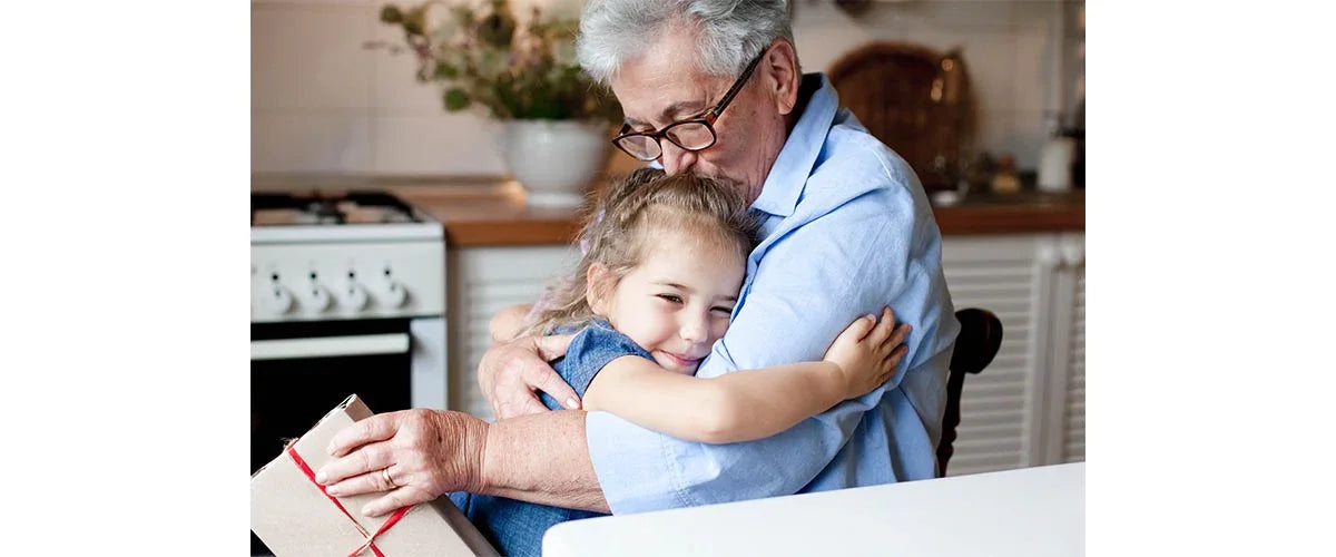 Senior wearing adaptive clothing from Ovidis hugs a young child in a cozy kitchen setting.