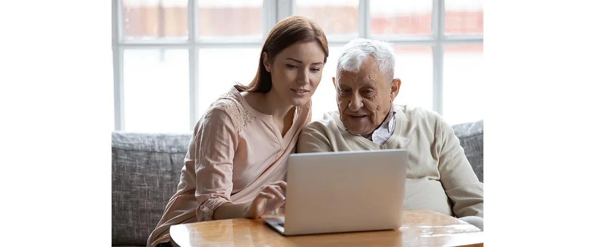 Caregiver helping senior man shop online for adaptive clothing on a laptop at home
