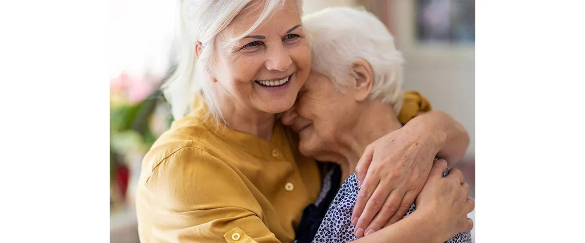Smiling senior woman hugging elderly loved one, promoting Ovidis adaptive clothing for dementia care.