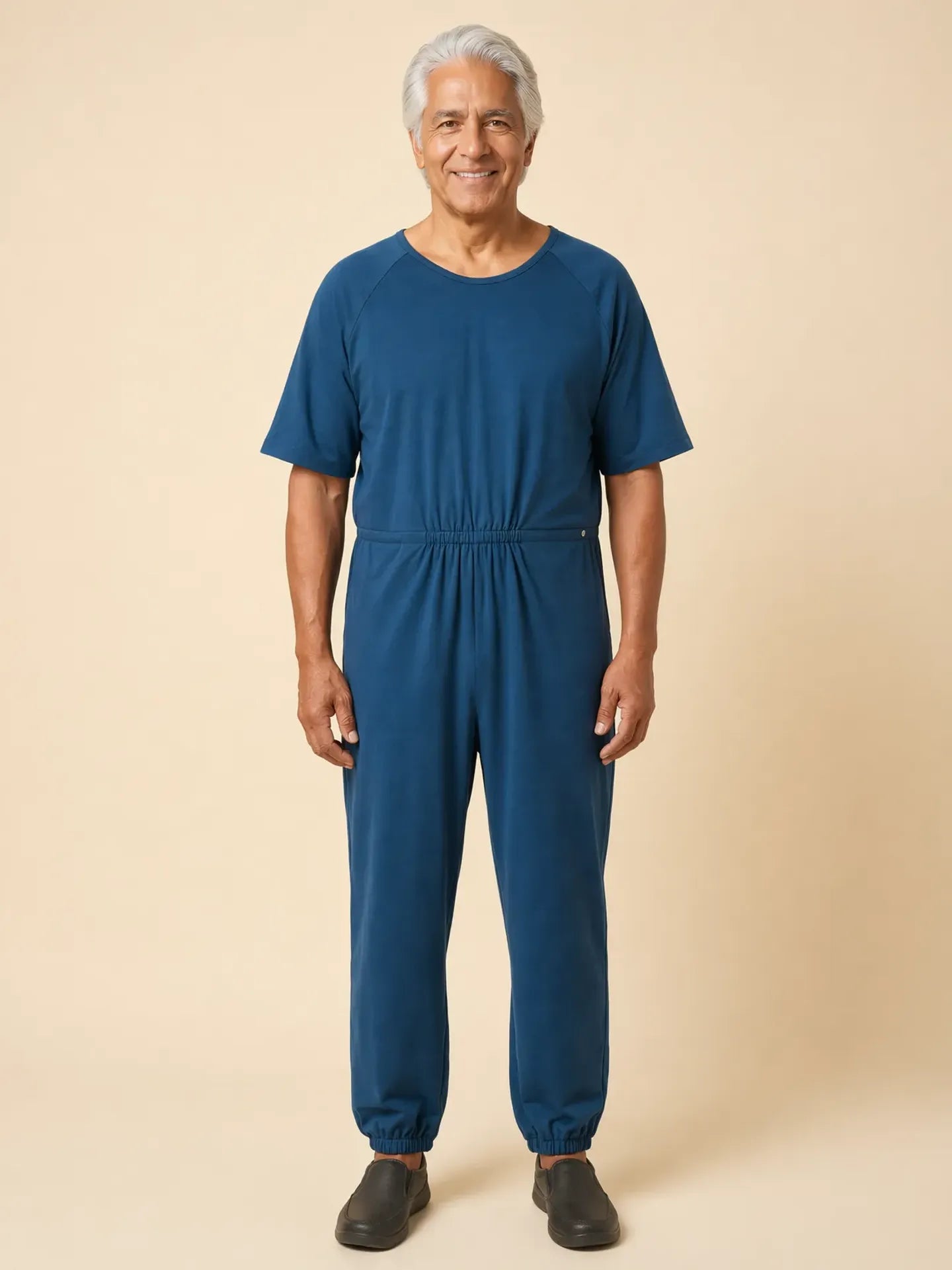 Senior man wearing Ovidis adaptive Bobby Teal jumpsuit, front view, warm studio lighting