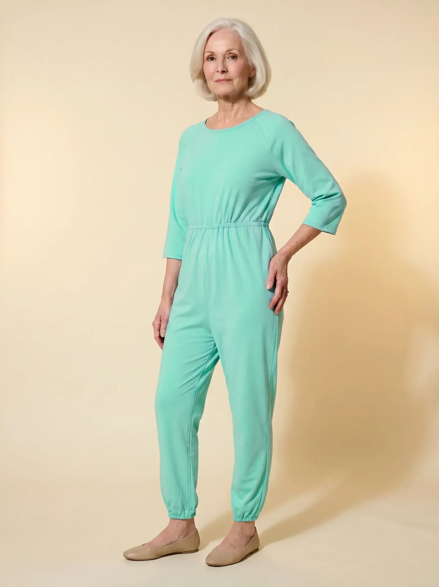 Senior woman wearing Ovidis adaptive mint green jumpsuit, front view, warm studio lighting