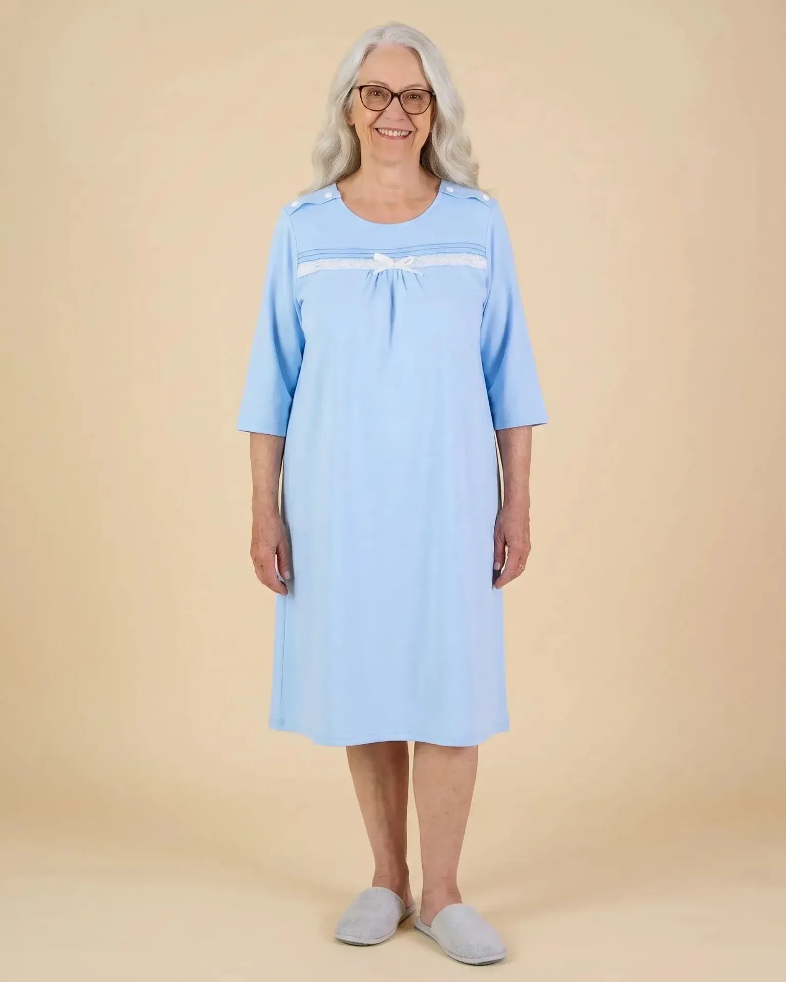 Senior woman wearing Ovidis Olivia adaptive nightgown in powder blue with lace and bow chest detail, full length, front view