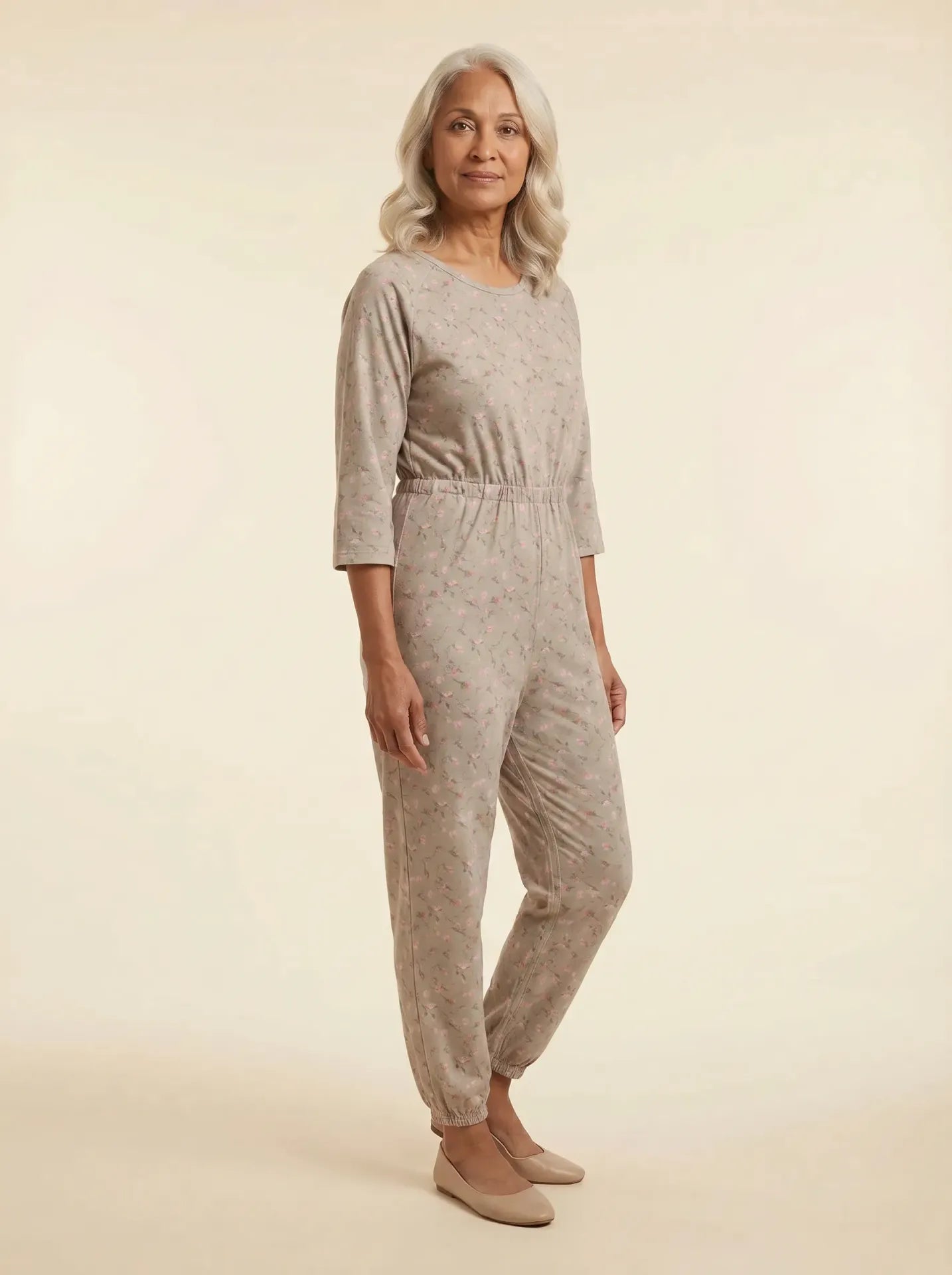 Senior woman wearing Ovidis adaptive taupe magnolia floral jumpsuit, front view, warm studio lighting