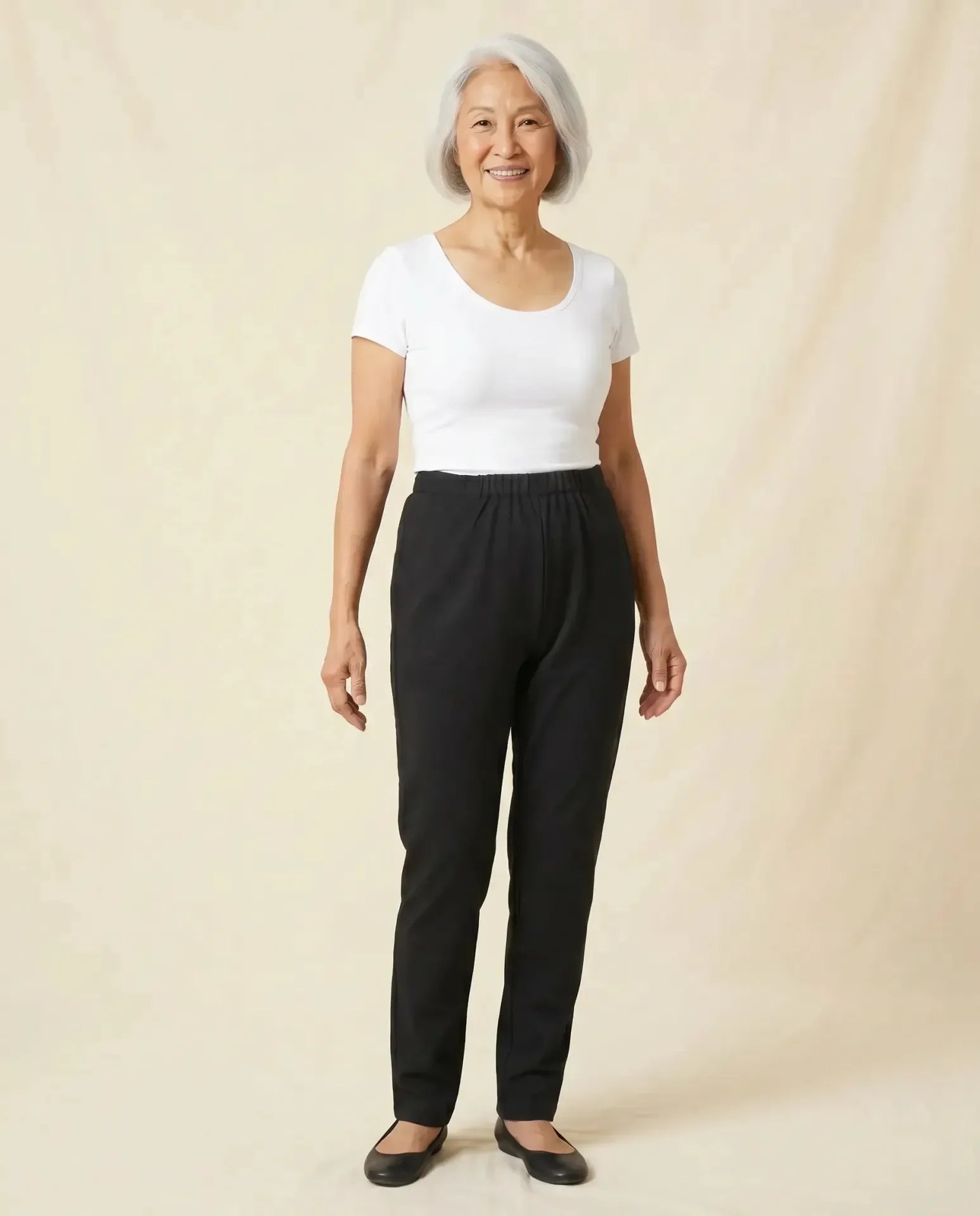 Senior Asian woman wearing Ovidis Arie Pants in Black, full body front view on parchment backdrop