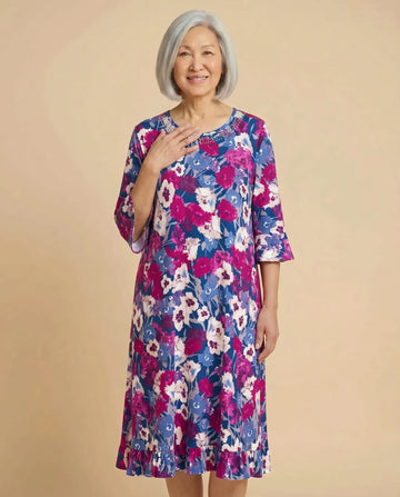 Senior Asian woman wearing Romei Fushia adaptive floral dress with bell sleeves, parchment backdrop