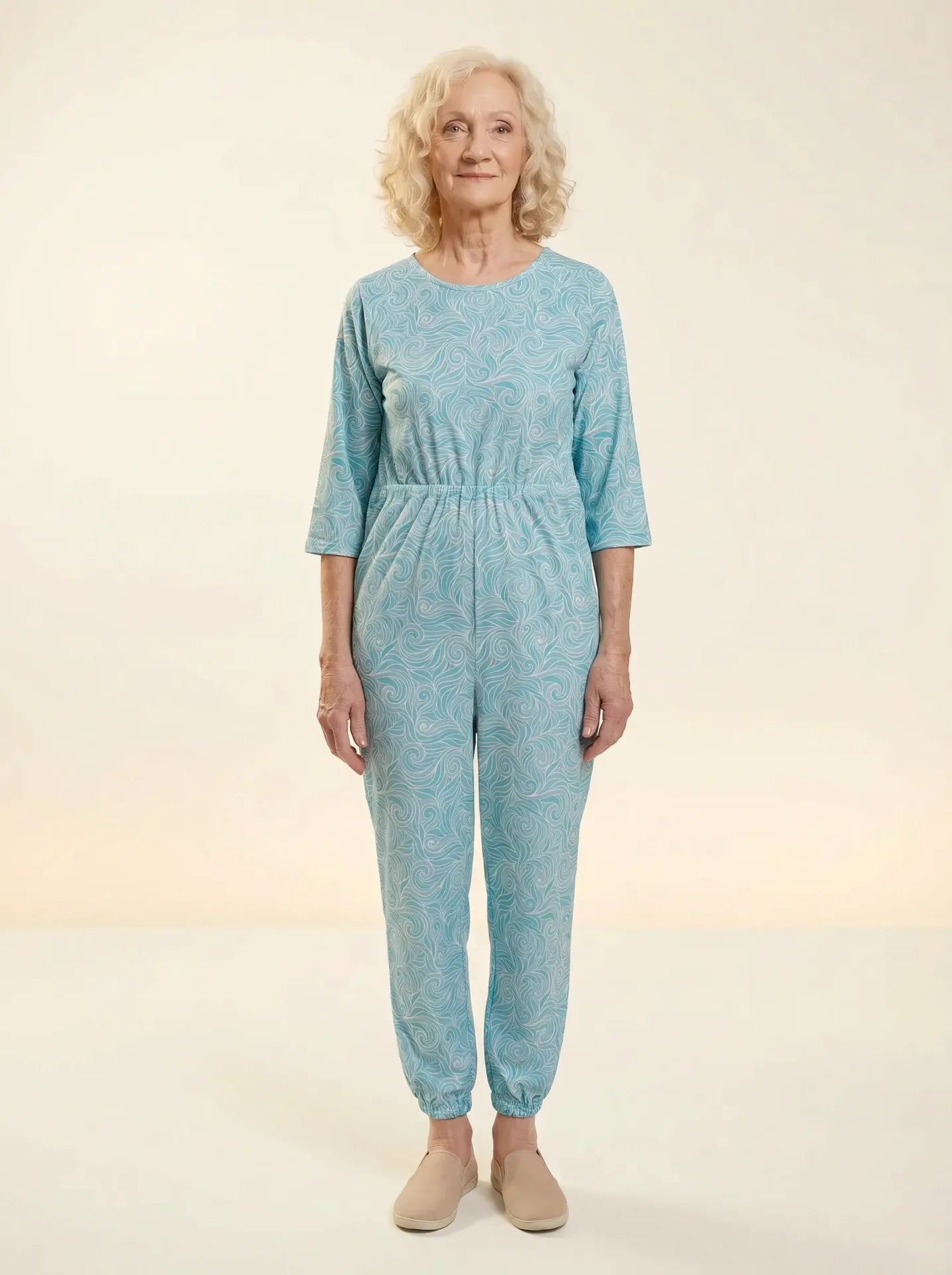 Senior woman wearing Ovidis adaptive swirls teal pattern jumpsuit, front view, warm studio lighting