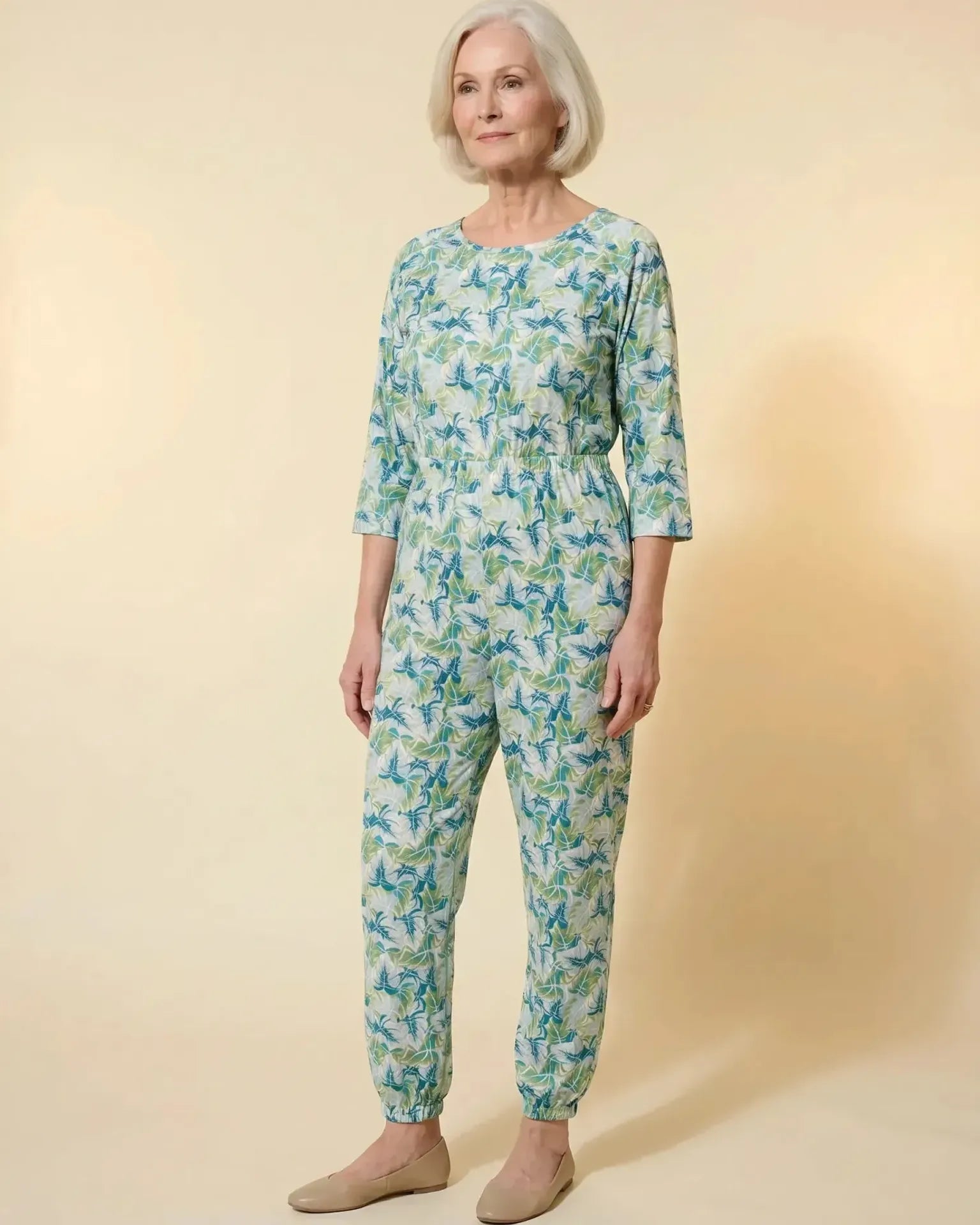 Senior woman wearing Ovidis adaptive Carrie Mint tropical leaf jumpsuit, full body front view