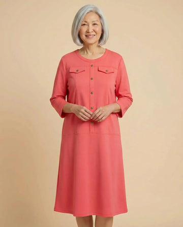 Senior Asian woman wearing Demi Coral adaptive ponte dress with brass buttons, parchment backdrop