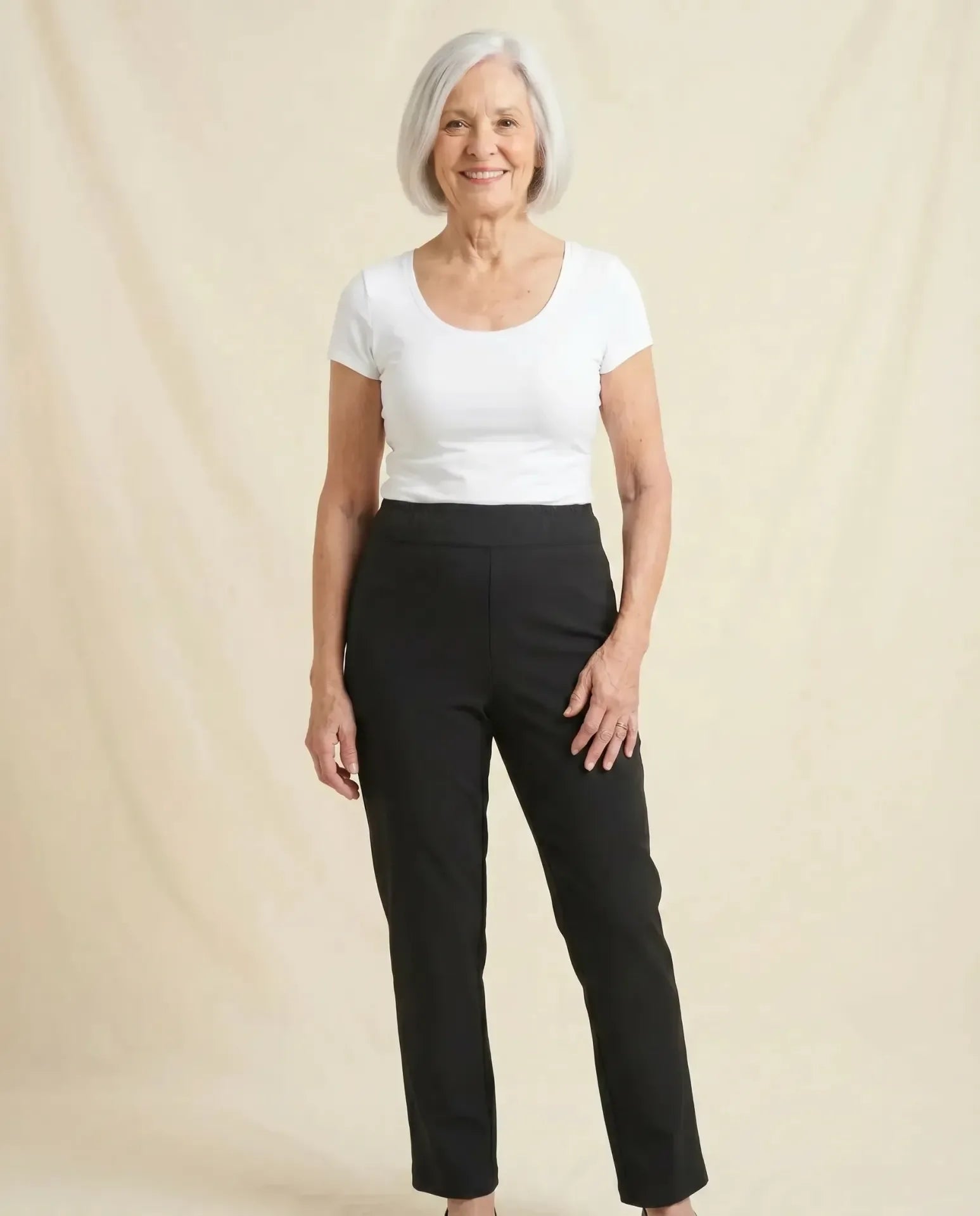 Senior woman wearing Ovidis Sara Pants in Black, full body front view on parchment backdrop