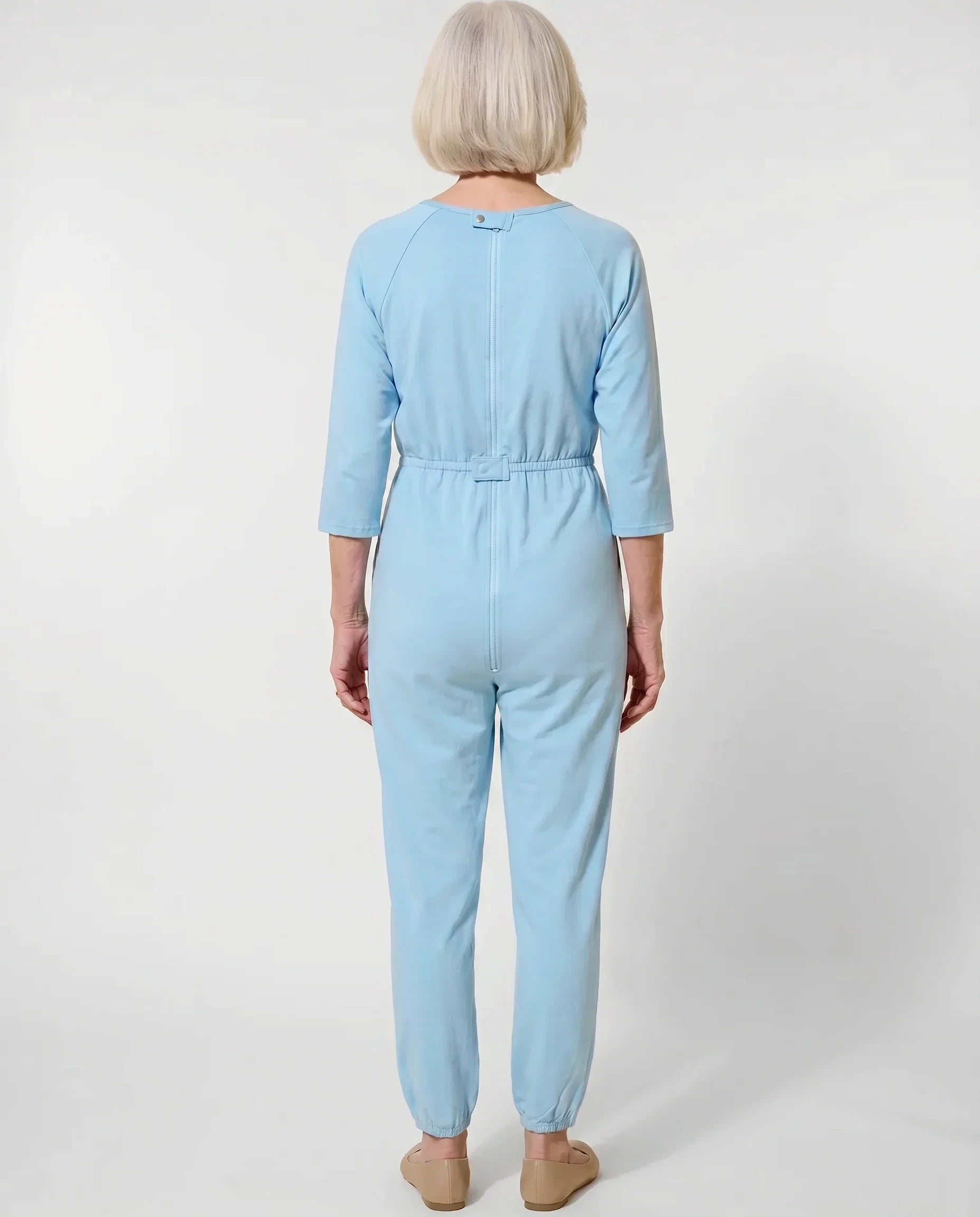 Senior woman wearing Ovidis adaptive Carrie Blue jumpsuit, full body back view showing center-back zipper and snap closures