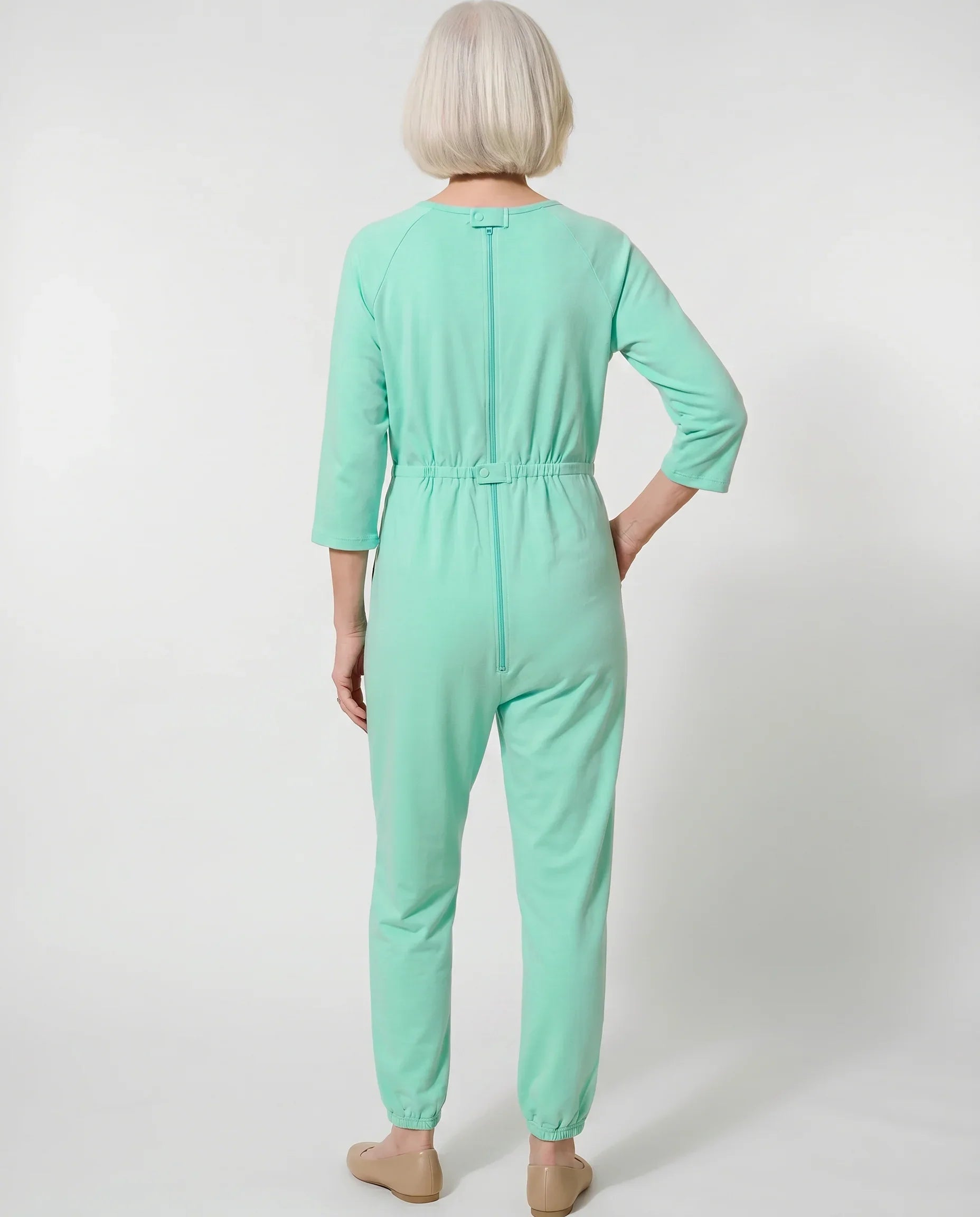 Senior woman wearing Ovidis adaptive Carrie Green jumpsuit, full body back view showing center-back zipper and snap closure