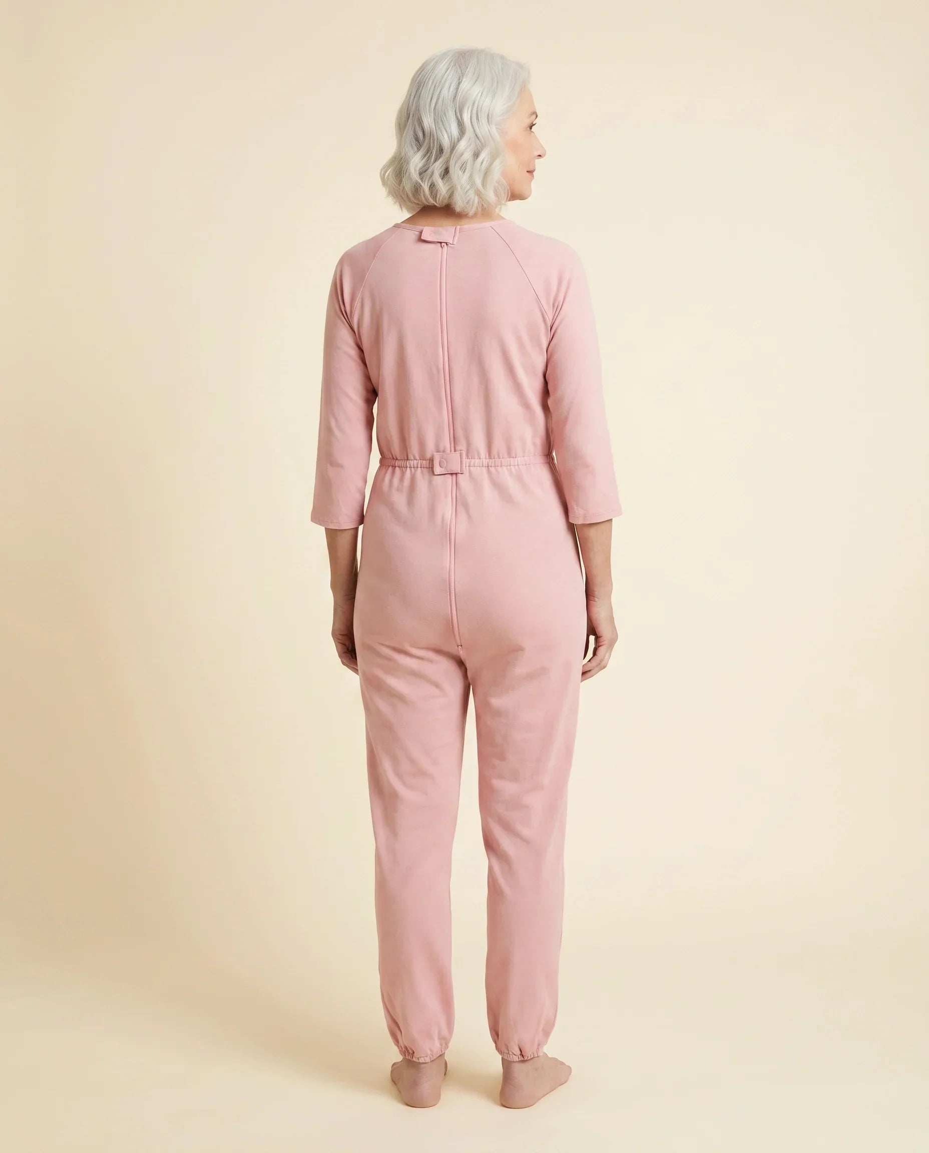 Senior woman wearing Ovidis Carrie Pink adaptive jumpsuit, back view showing full-length zipper and snap closure