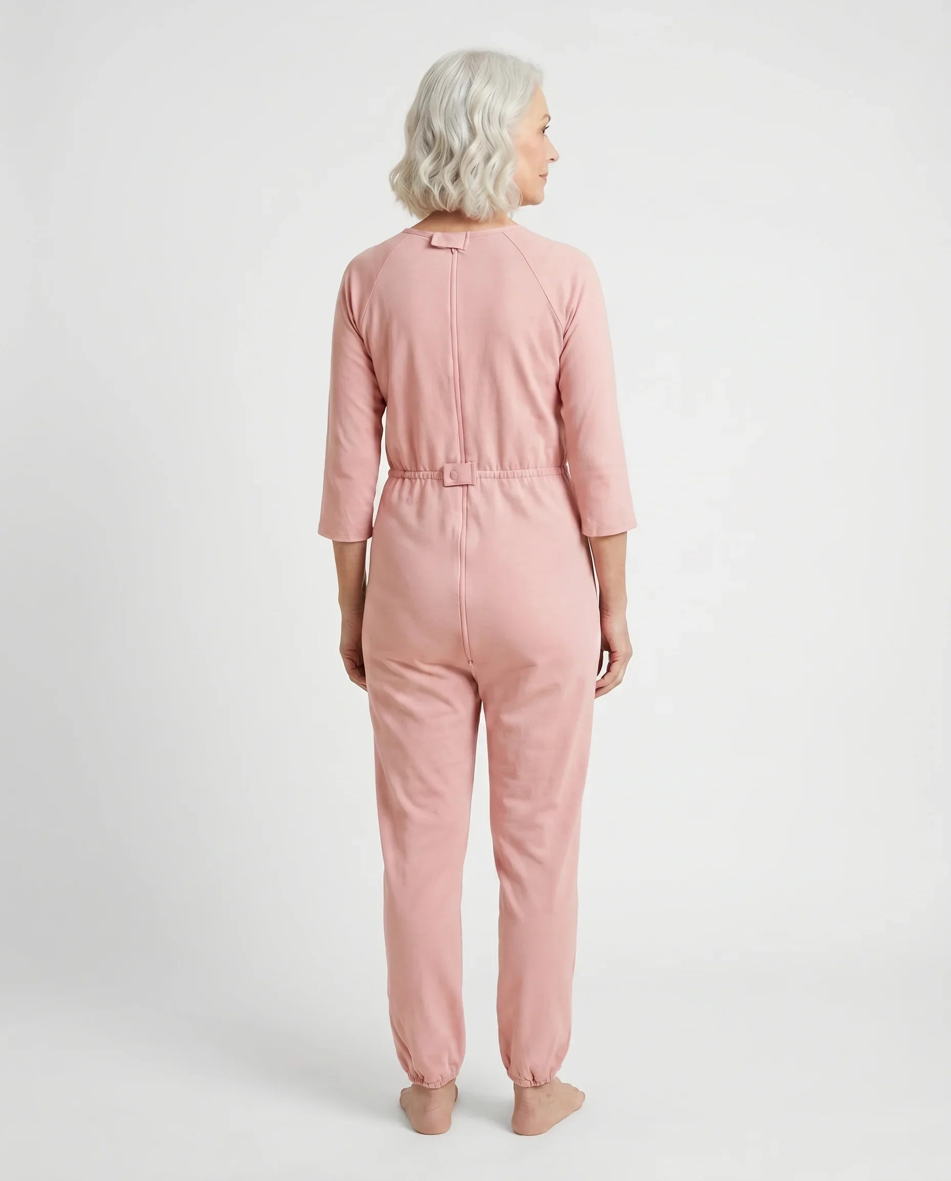 Senior woman wearing Ovidis Carrie Pink adaptive jumpsuit, back view showing full-length zipper and snap closure