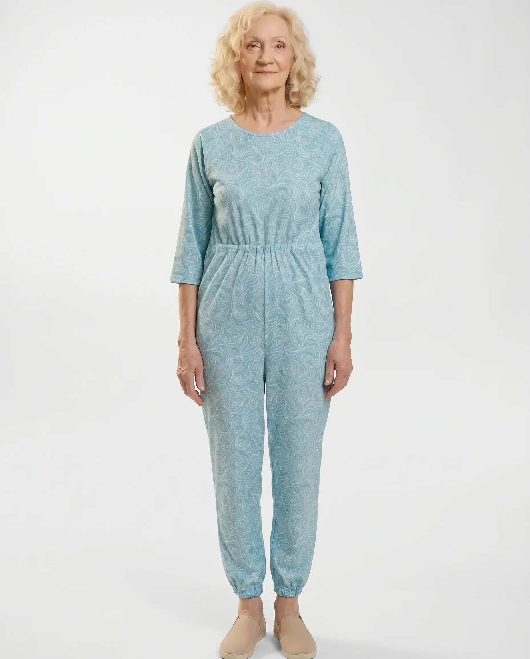 Senior woman wearing Ovidis adaptive Carrie Swirls teal jumpsuit, full body front view