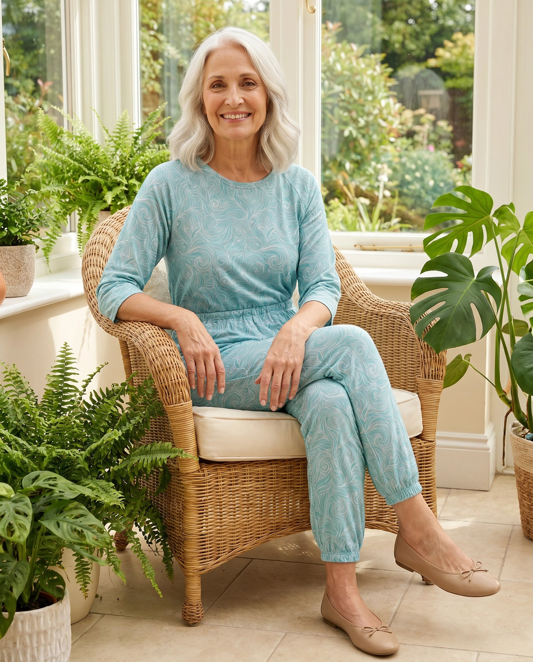Senior woman wearing Ovidis adaptive Carrie Swirls jumpsuit in sunroom, care facility lifestyle
