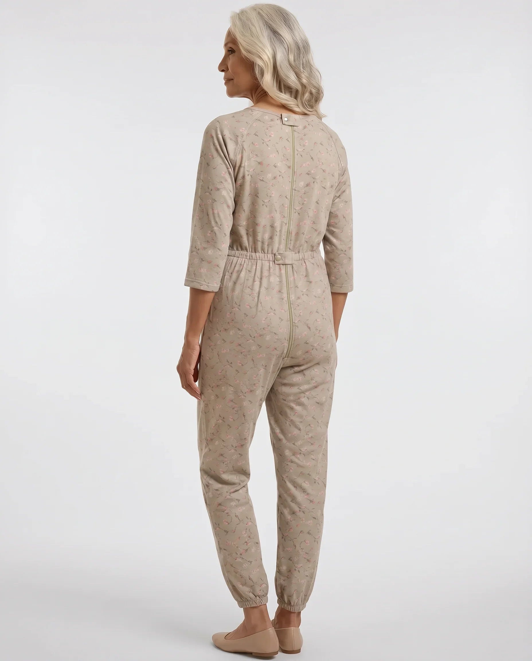 Senior woman wearing Ovidis adaptive Carrie Taupe floral jumpsuit, full body back view showing center-back zipper and snap closure