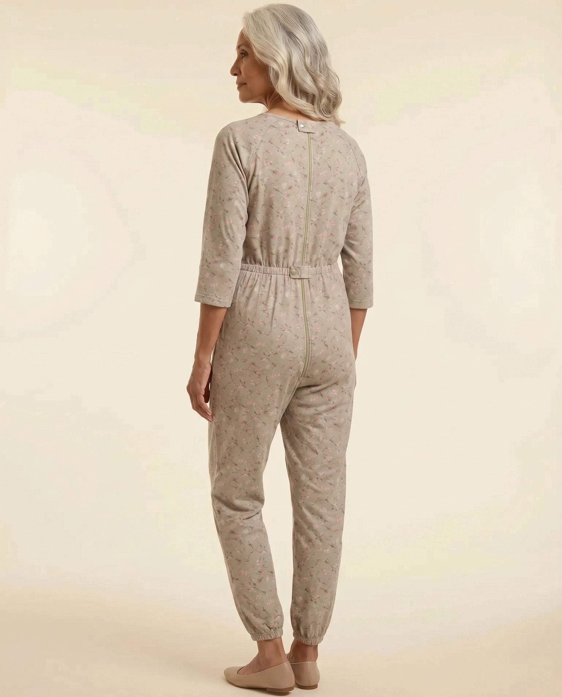 Senior woman wearing Ovidis adaptive Carrie Taupe floral jumpsuit, full body back view showing center-back zipper and snap closures