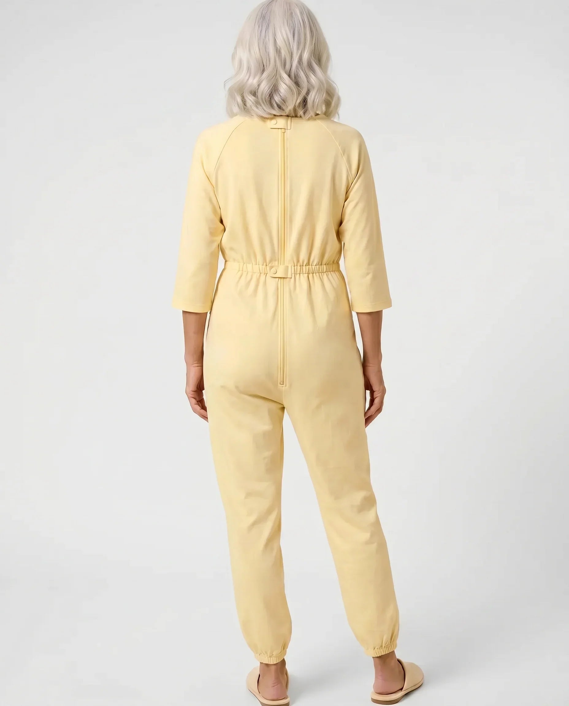 Senior woman wearing Ovidis adaptive Carrie Yellow jumpsuit, full body back view showing center-back zipper and snap closure