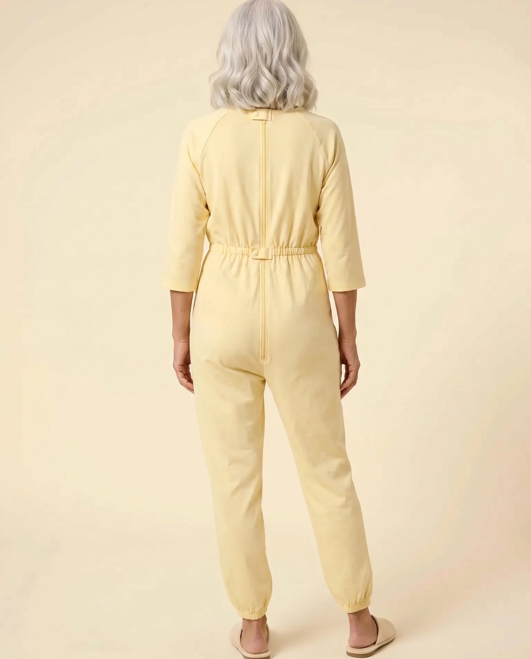 Senior woman wearing Ovidis adaptive Carrie Yellow jumpsuit, full body back view showing center-back zipper and snap closures