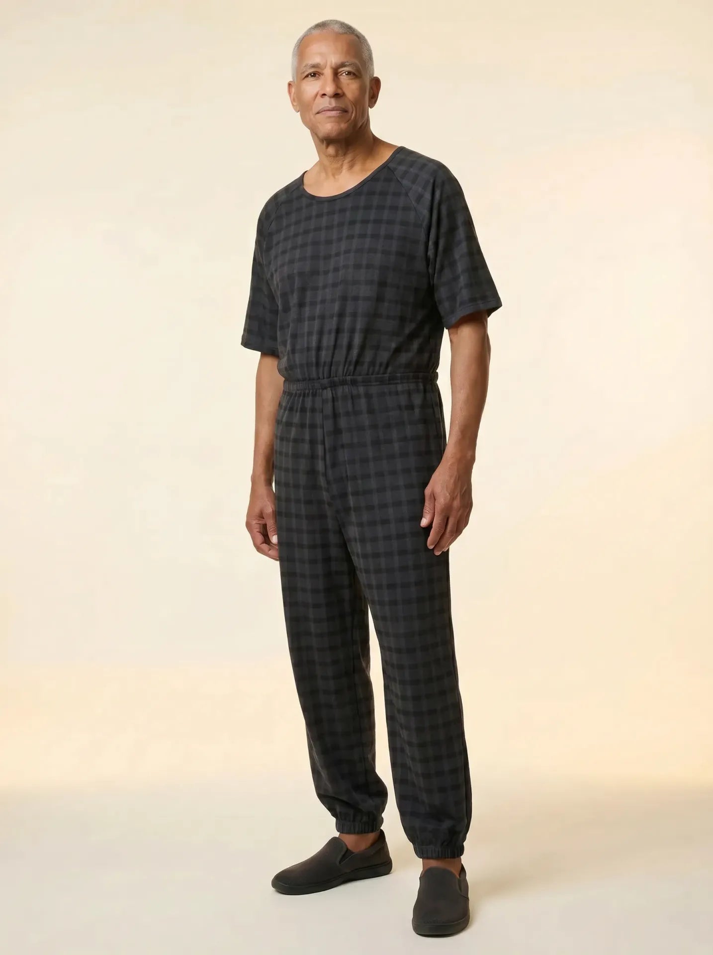 Senior man wearing Ovidis adaptive Bobby Black Check jumpsuit, front view, warm studio lighting