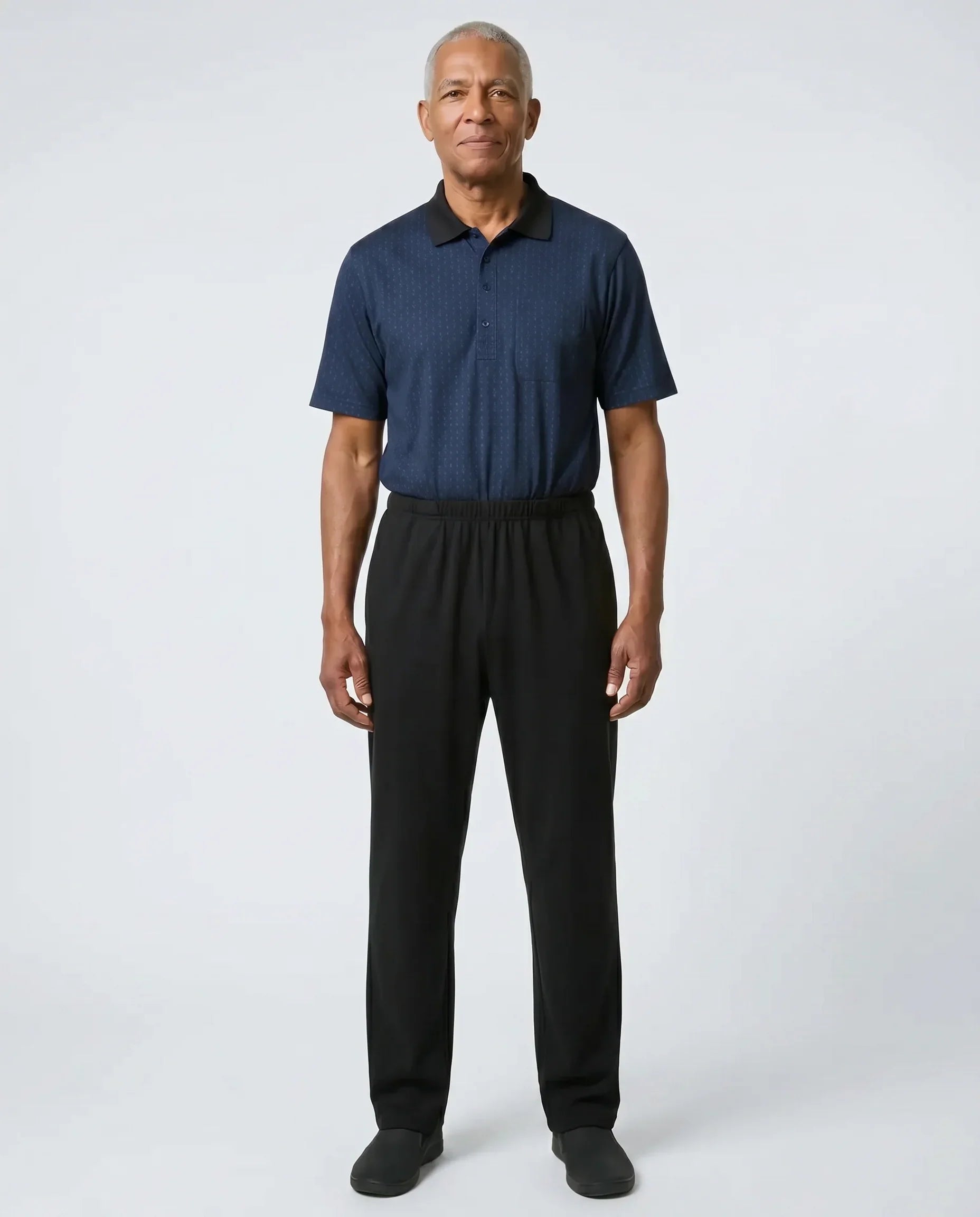 Senior man wearing Charly Twilight adaptive jumpsuit — deep midnight navy micro-pattern polo top with black pants