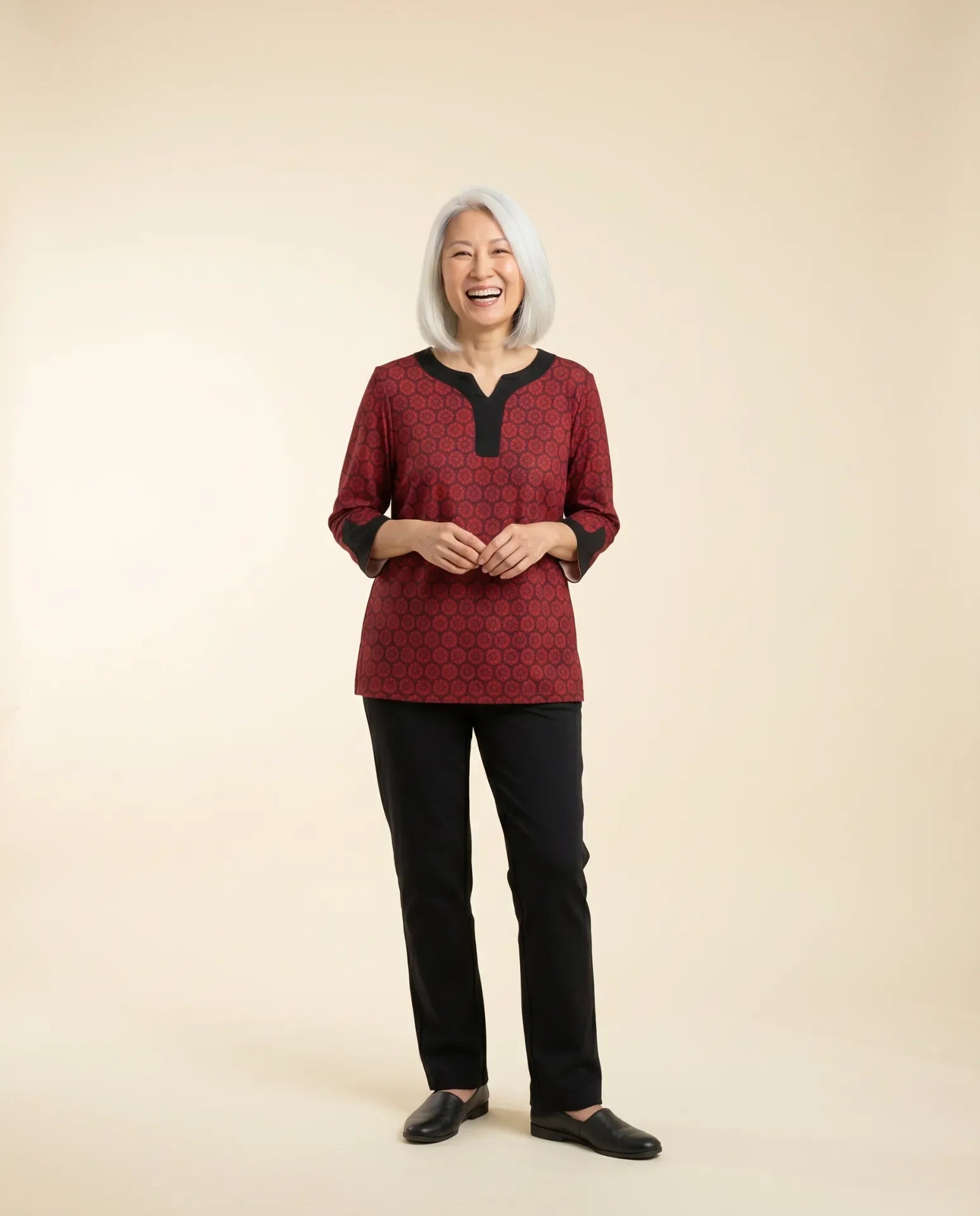 Senior woman wearing adaptive garnet red floral-print top with contrast black collar and sleeve trim, paired with black pants