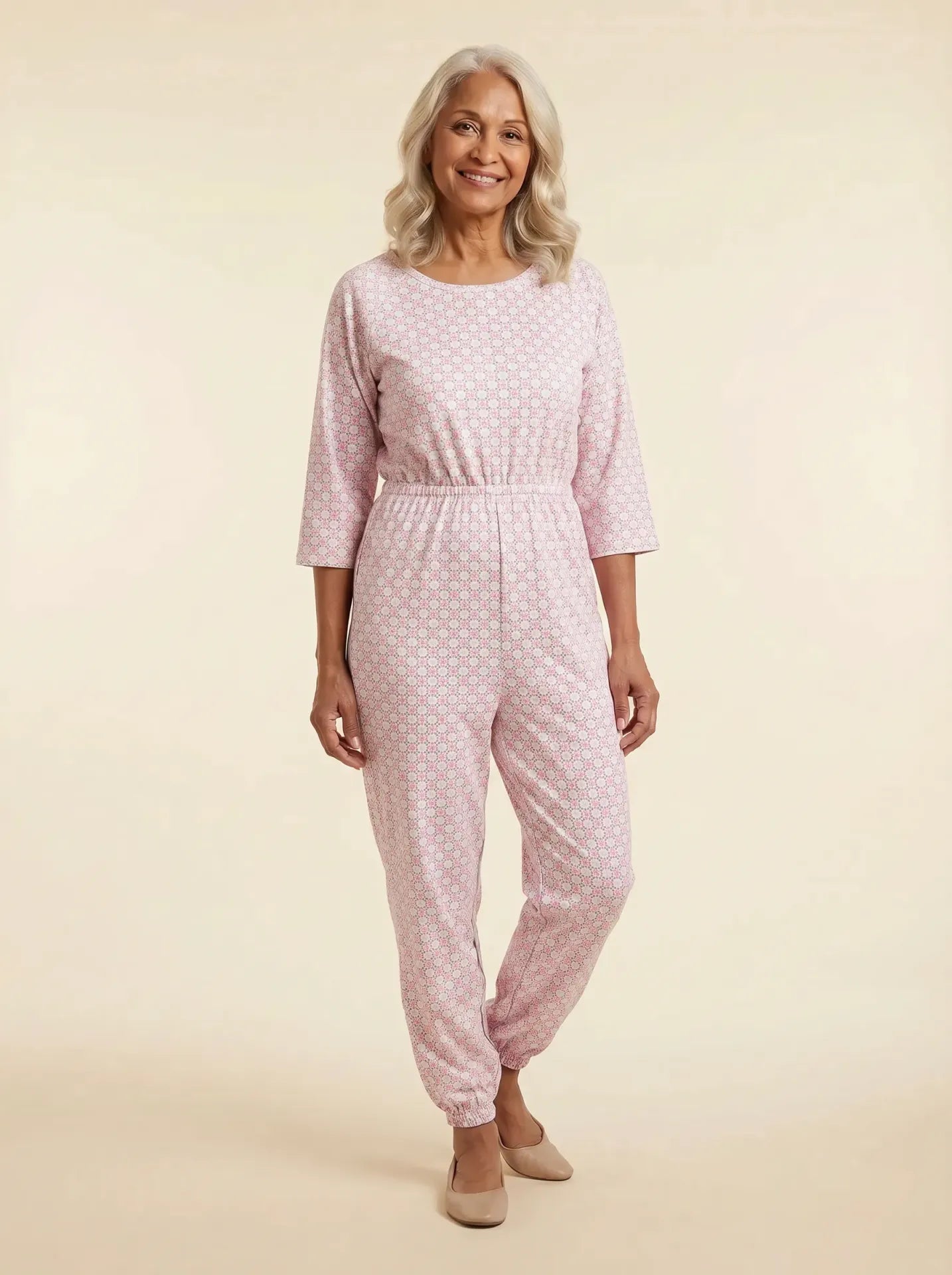 Senior woman wearing Ovidis adaptive blush geometric print jumpsuit, front view, warm studio lighting
