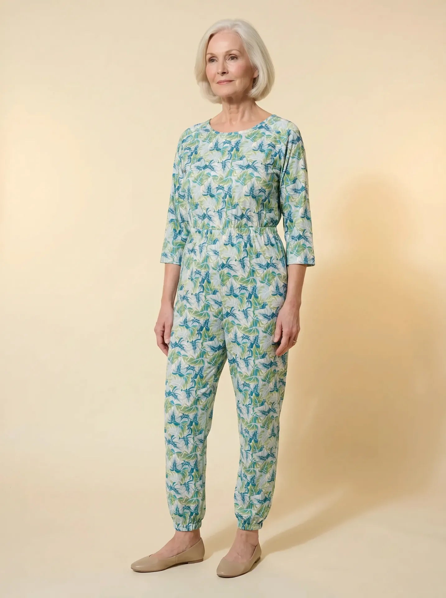 Senior woman wearing Ovidis adaptive mint tropical leaf print jumpsuit, front view, warm studio lighting