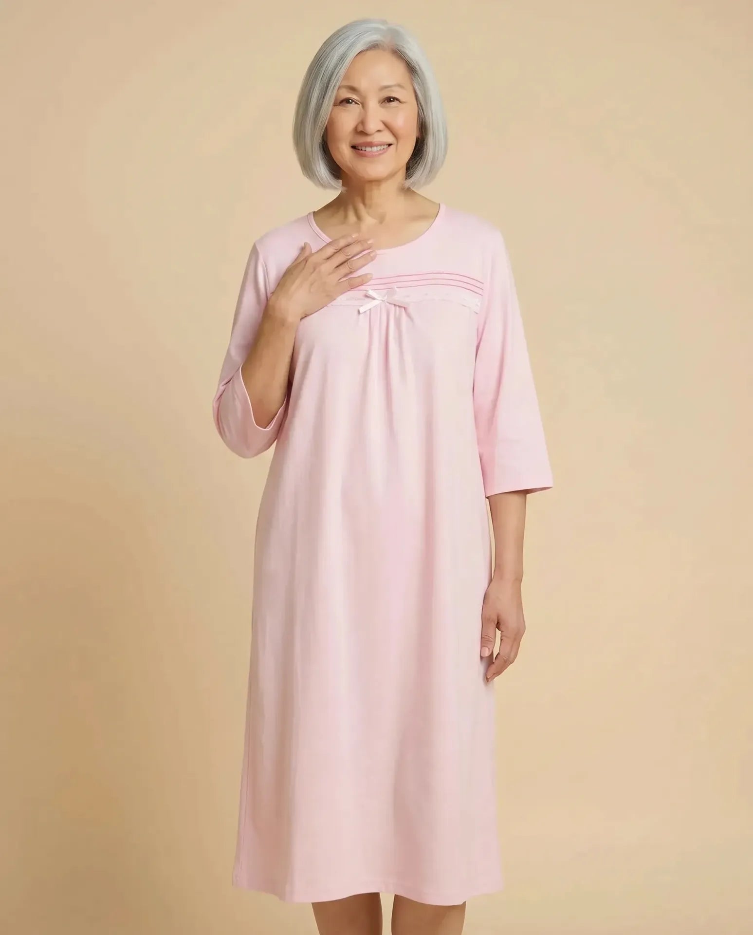 Senior woman wearing Olivia Nightgown in Pink, hand on chest pose, parchment backdrop