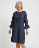 Senior woman wearing Loulou adaptive denim dress with ruffle placket and bell sleeves, front view