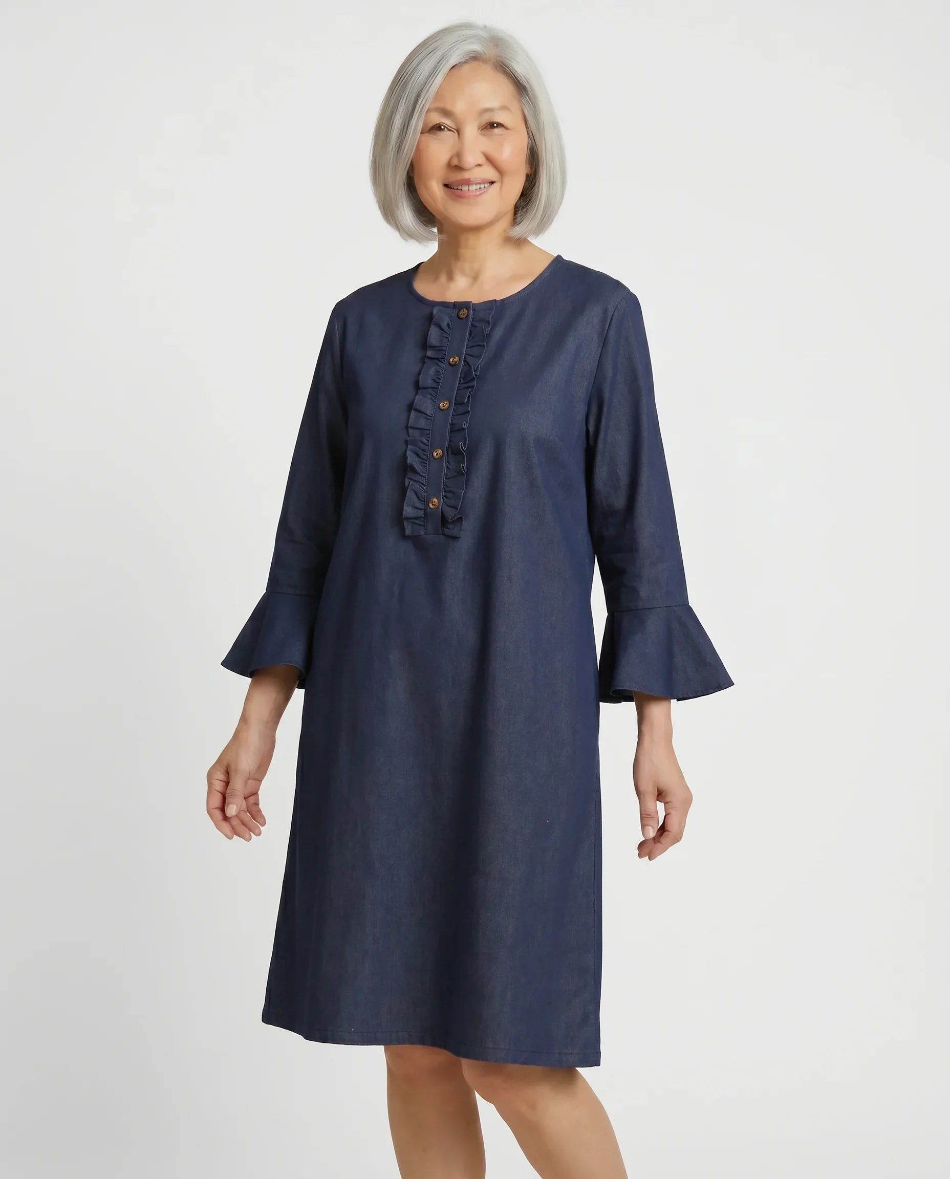 Senior woman wearing Loulou adaptive denim dress with ruffle placket and bell sleeves, front view