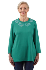 Senior woman wearing a mint green adaptive long sleeve shirt with embroidered neckline
